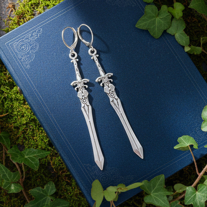 Silver sword-shaped earrings on a blue book with green leaves around