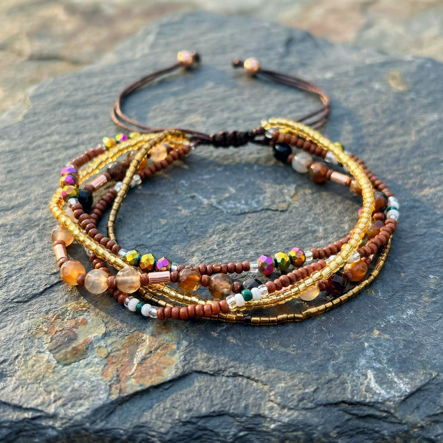 A multiple bead bracelet with gold and brown beads on a grey stone surface. Boho hippie style