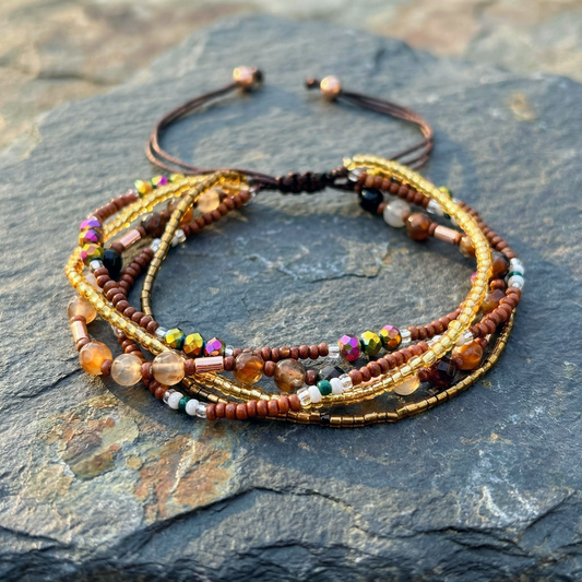 A multiple bead bracelet with gold and brown beads on a grey stone surface. Boho hippie style