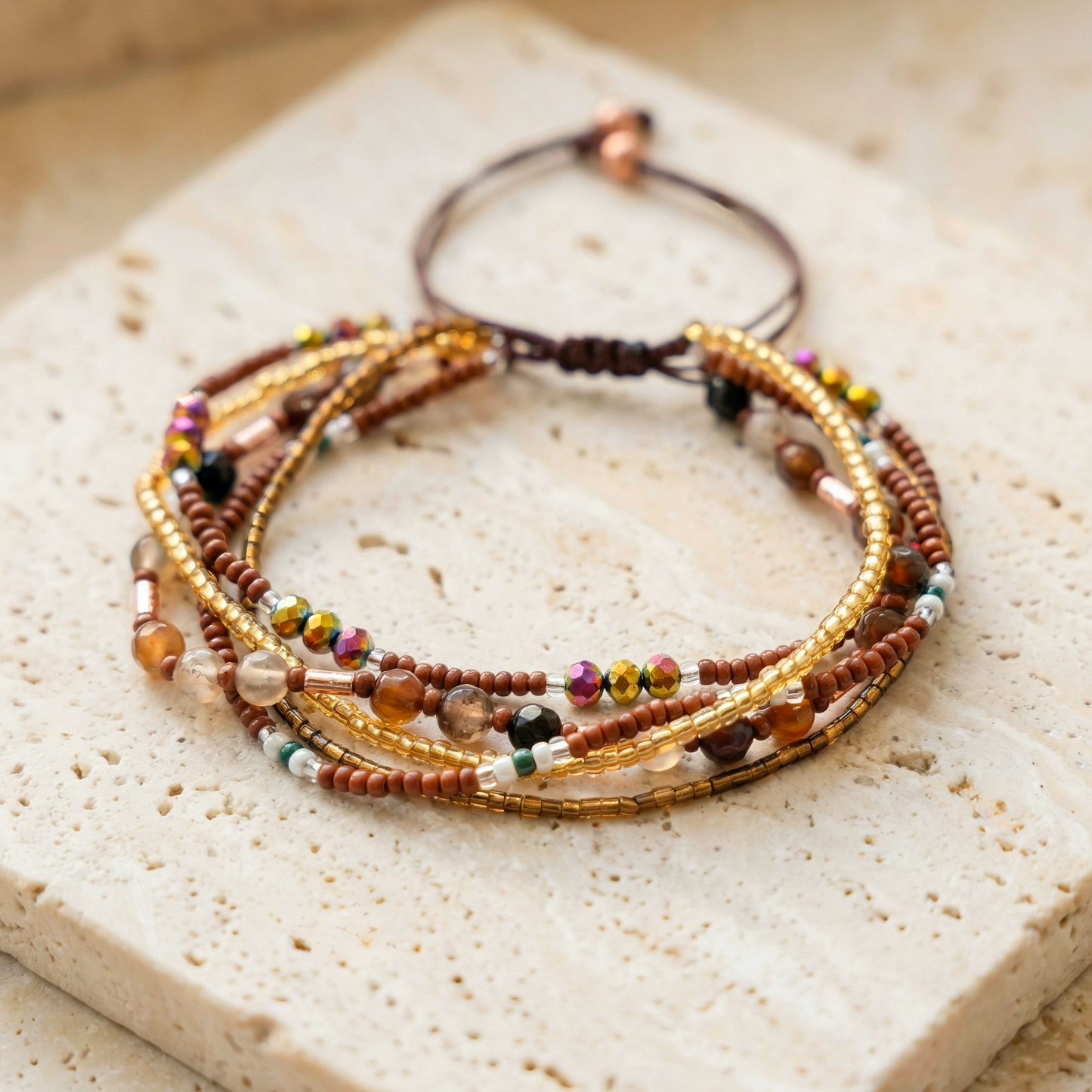 Multiple beaded bracelet with 5 layers of gold and brown beads tied together, on a light stone background. Boho rustic style