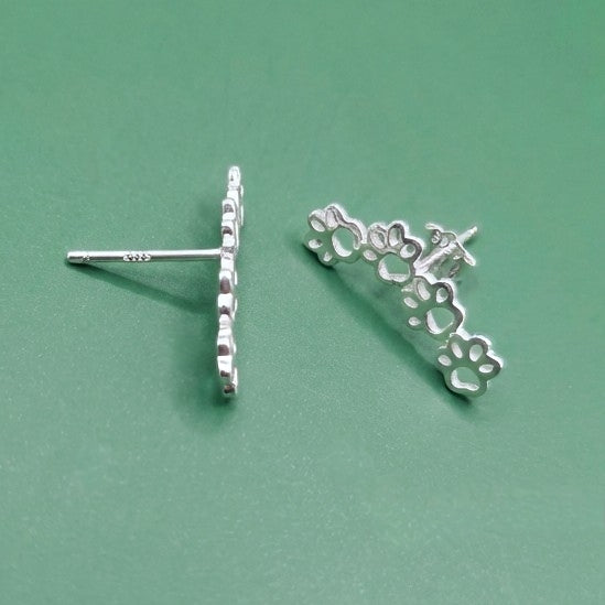 Silver dog paw earrings on a green background
