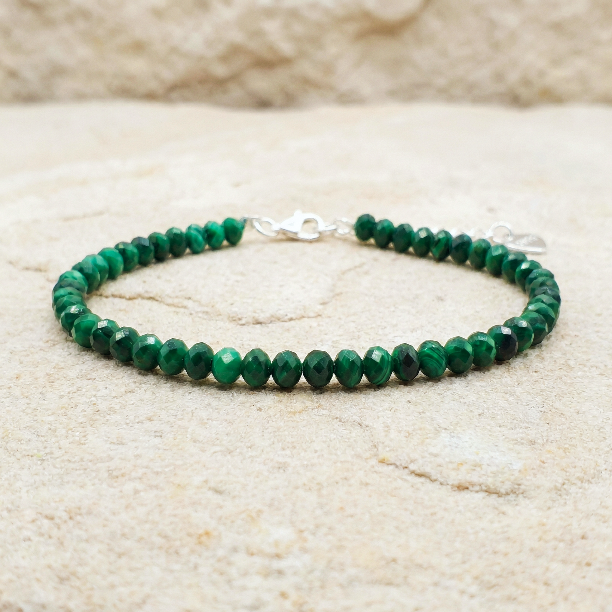 Natural green malachite bead bracelet with a 925 silver clasp on a light stone background