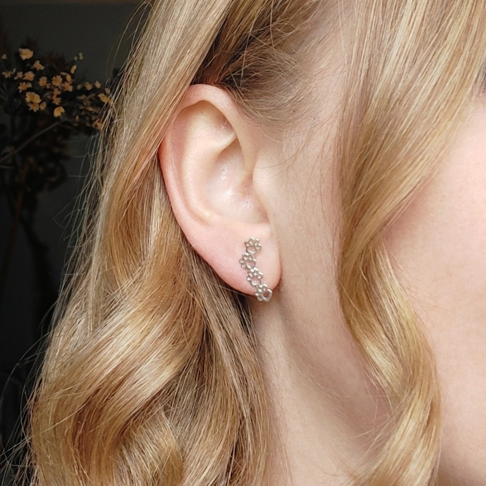 Close-up of an ear wearing a delicate paw stud earring with blonde hair.