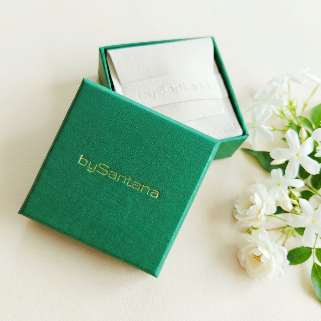 Green jewelry box with 'bySantana' branding on a light background with white flowers.