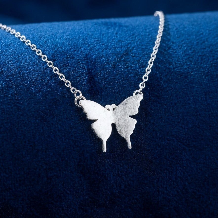 Silver butterfly necklace with a matte brushed effect on a blue background