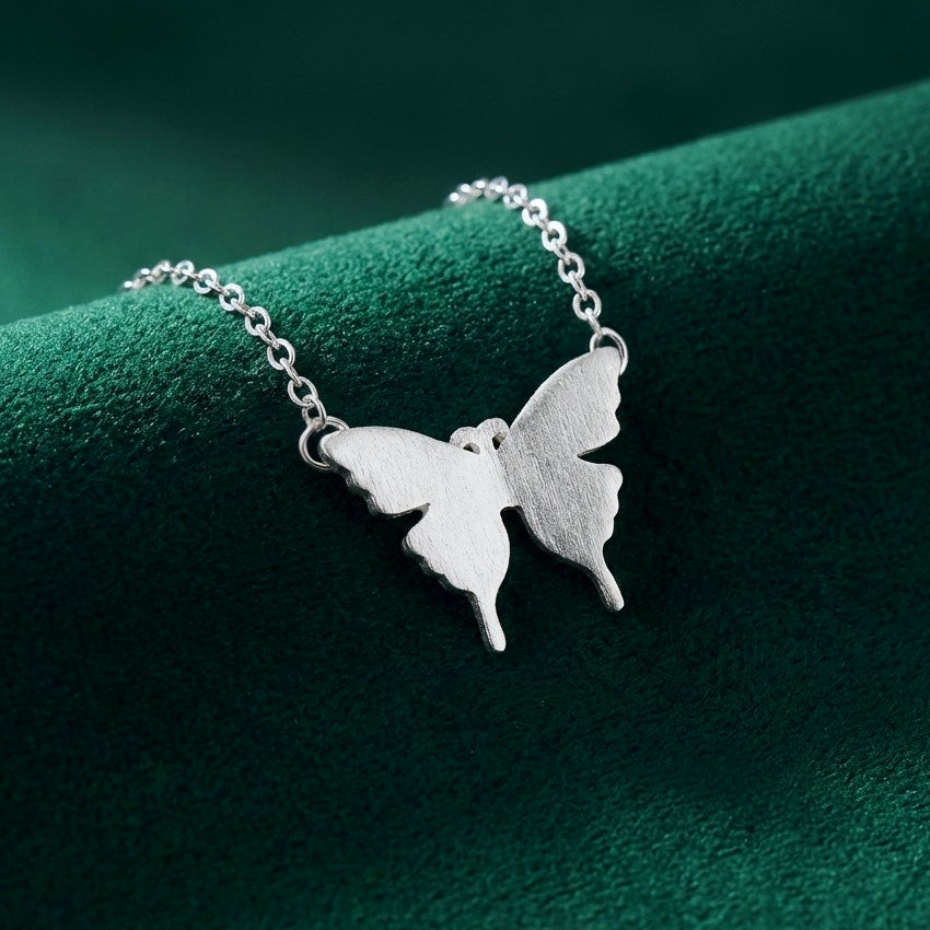 Silver butterfly necklace on a green textured surface
