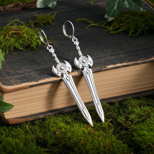 Sci fi fantasy silver sword earrings with hoops on a book with moss