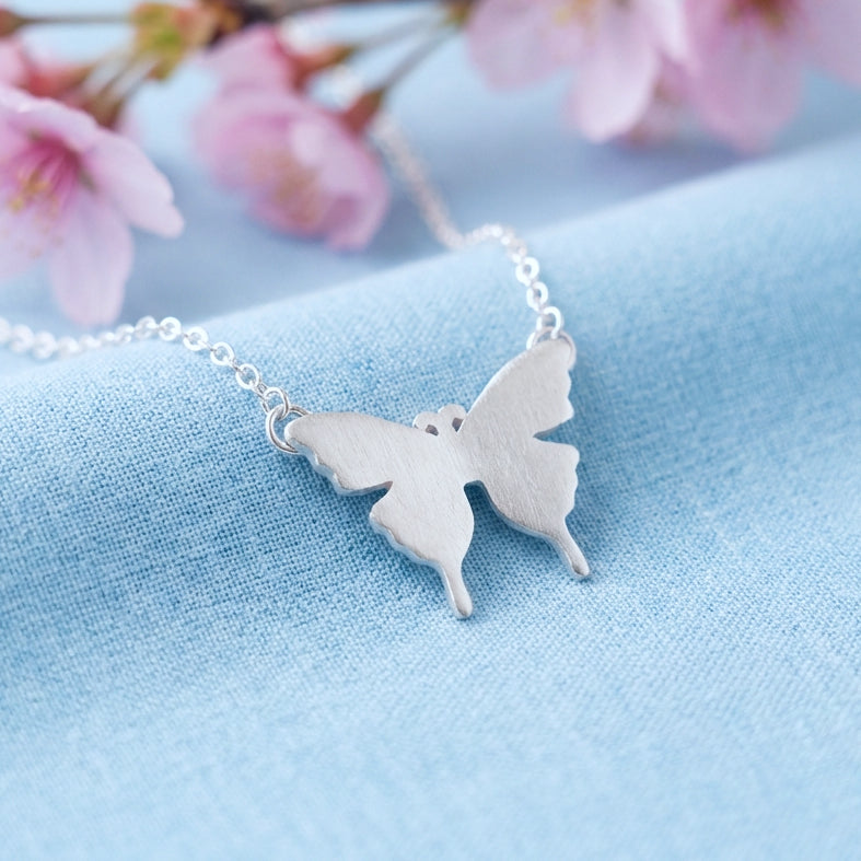 Silver butterfly necklace on a light blue fabric background with pink flowers.