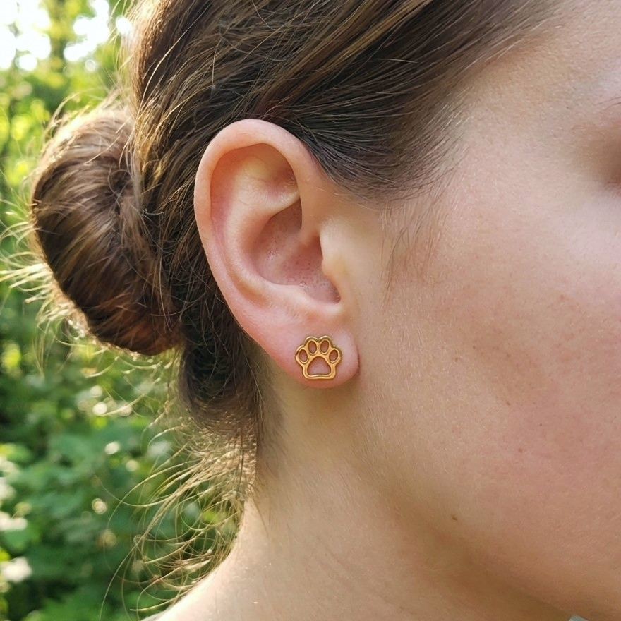 Gold paw print earring worn by a person with a blurred green background