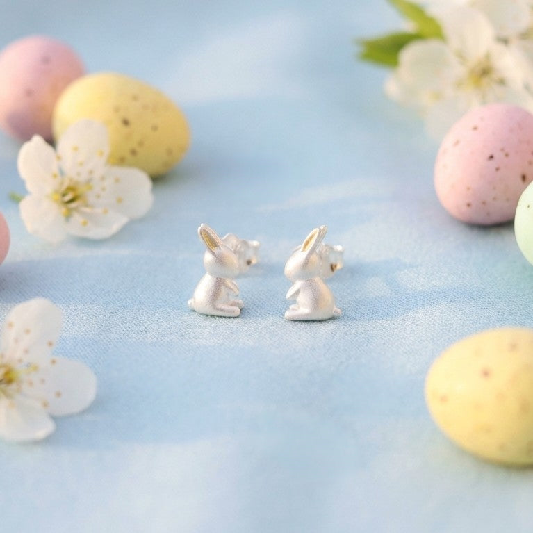 Silver bunny earrings on a light blue background with Easter eggs and flowers.