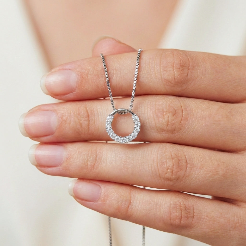 A hand holding a small sparkly round circle 925 silver pendant with crystals with a box chain necklace 