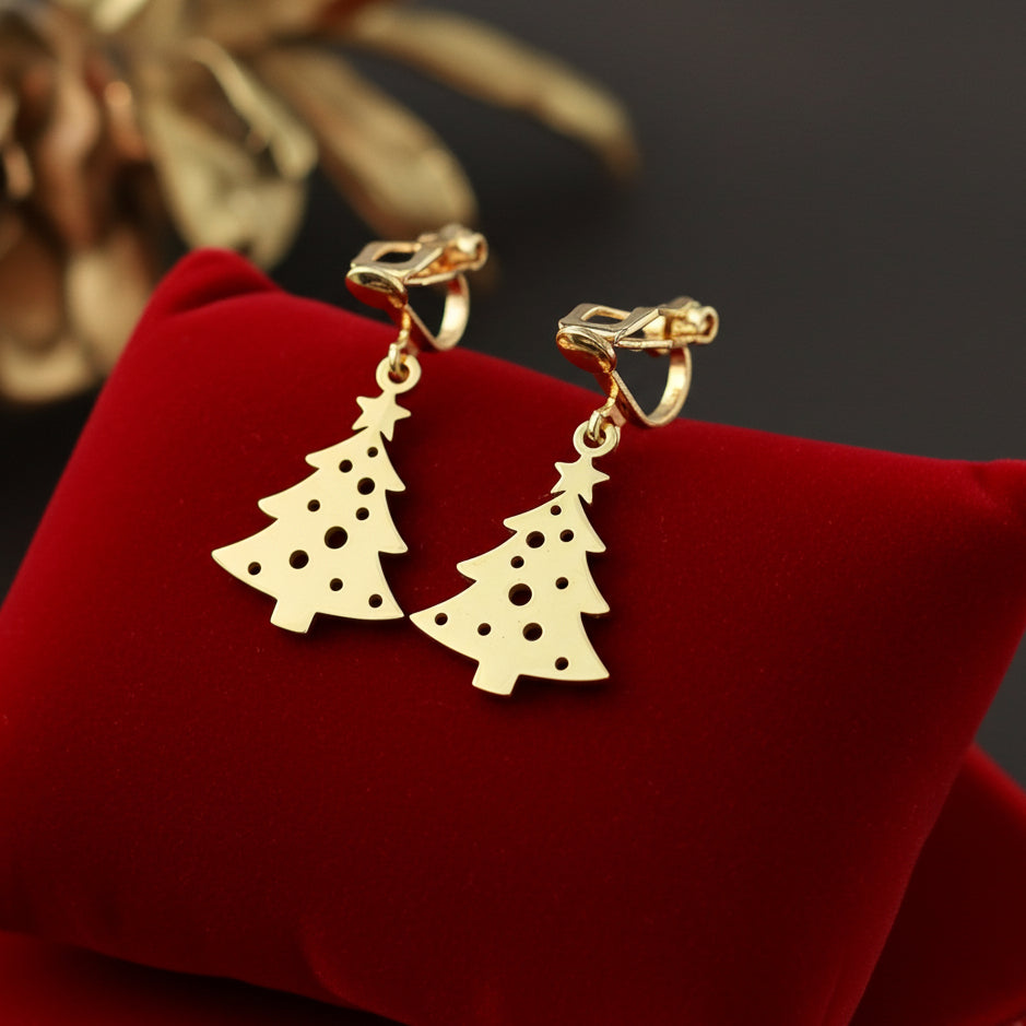 Festive Christmas tree earrings with clip-ons made from gold stainless steel on red velvet with lights in the background.