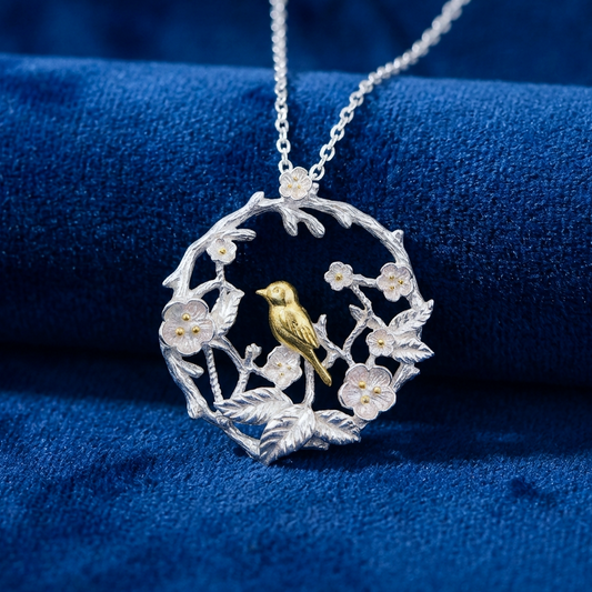 Silver pendant with a gold bird design in a circle of flowers on a blue fabric background