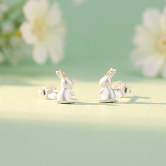 Cute silver bunny stud earrings on a light green background. They have gold ears. Spring/easter theme