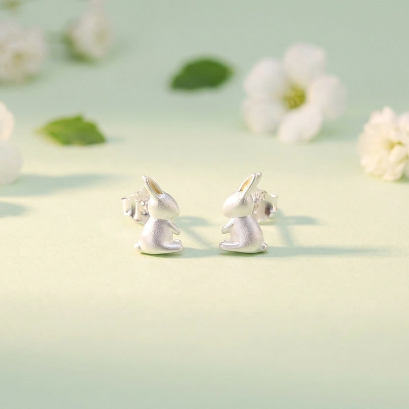 Silver bunny rabbit earrings on a light green background with flowers