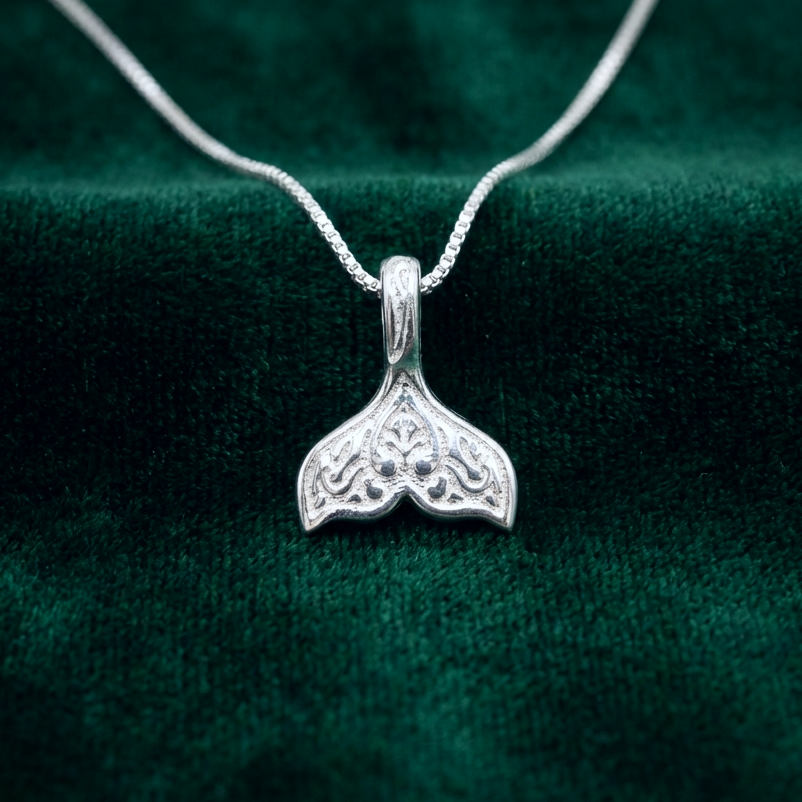 A silver whale tail necklace on a green background