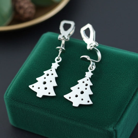 Festive Christmas tree earrings with clip-ons made from silver stainless steel on green velvet with lights in the background.