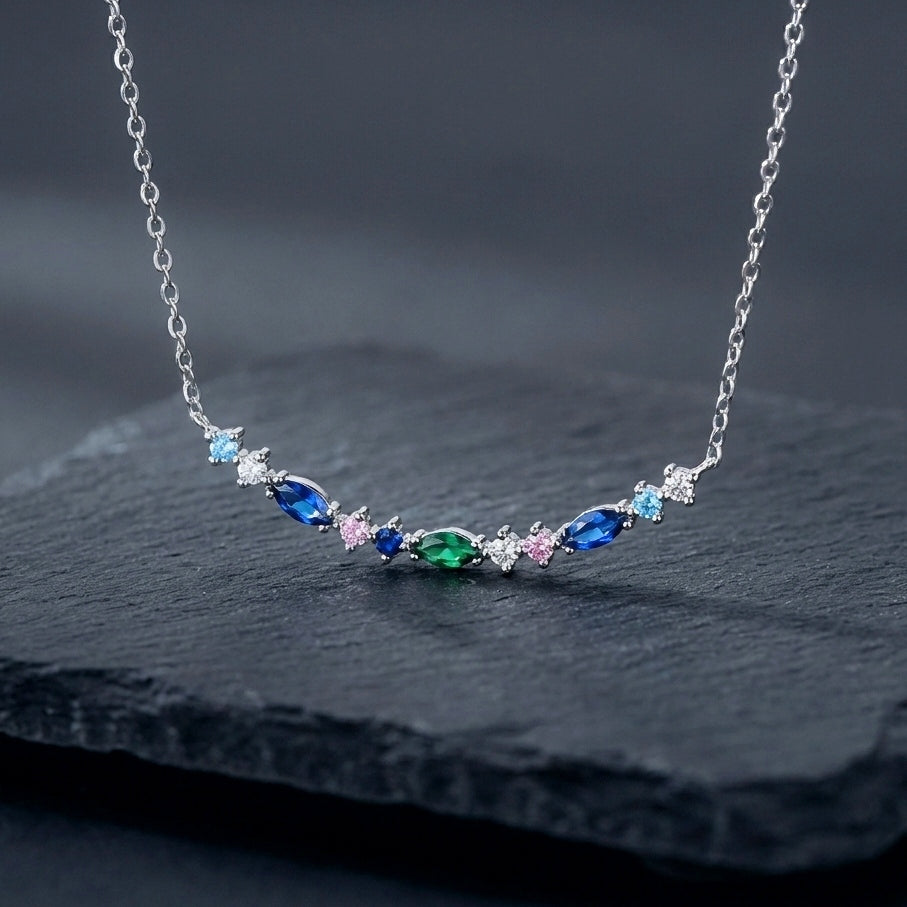 A dainty 925 silver bar pendant with blue and green gemstones in marquise and round shapes on a dark background.