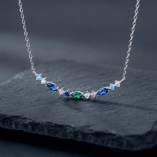 A dainty 925 silver bar pendant with blue and green gemstones in marquise and round shapes on a dark background.