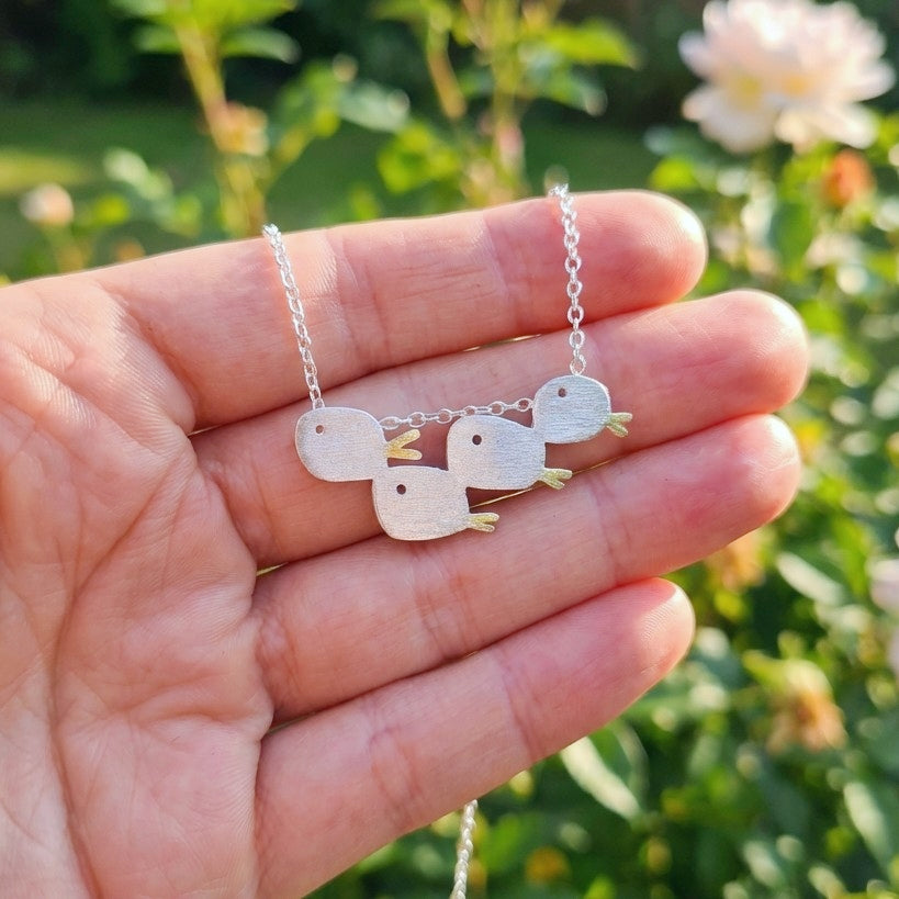A and holding a matte brushed silver necklace with a school of four fishes outside