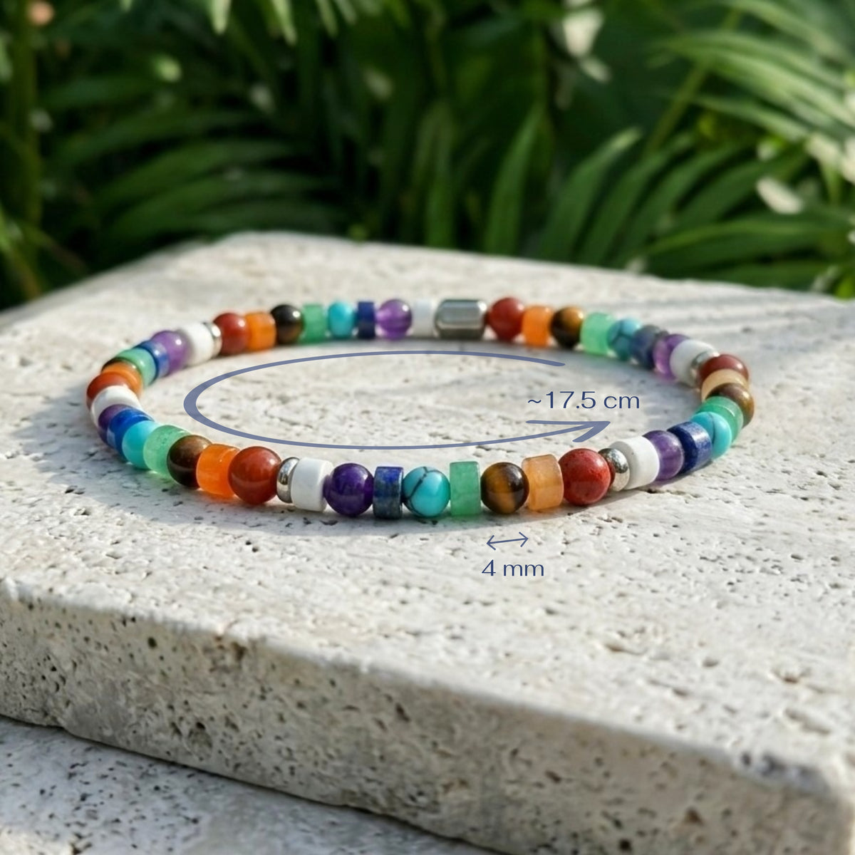 A multi gemstone beaded bracelet displayed on a light stone slab with green foliage in the background. Blue measurement annotations indicate a circumference of approximately 17.