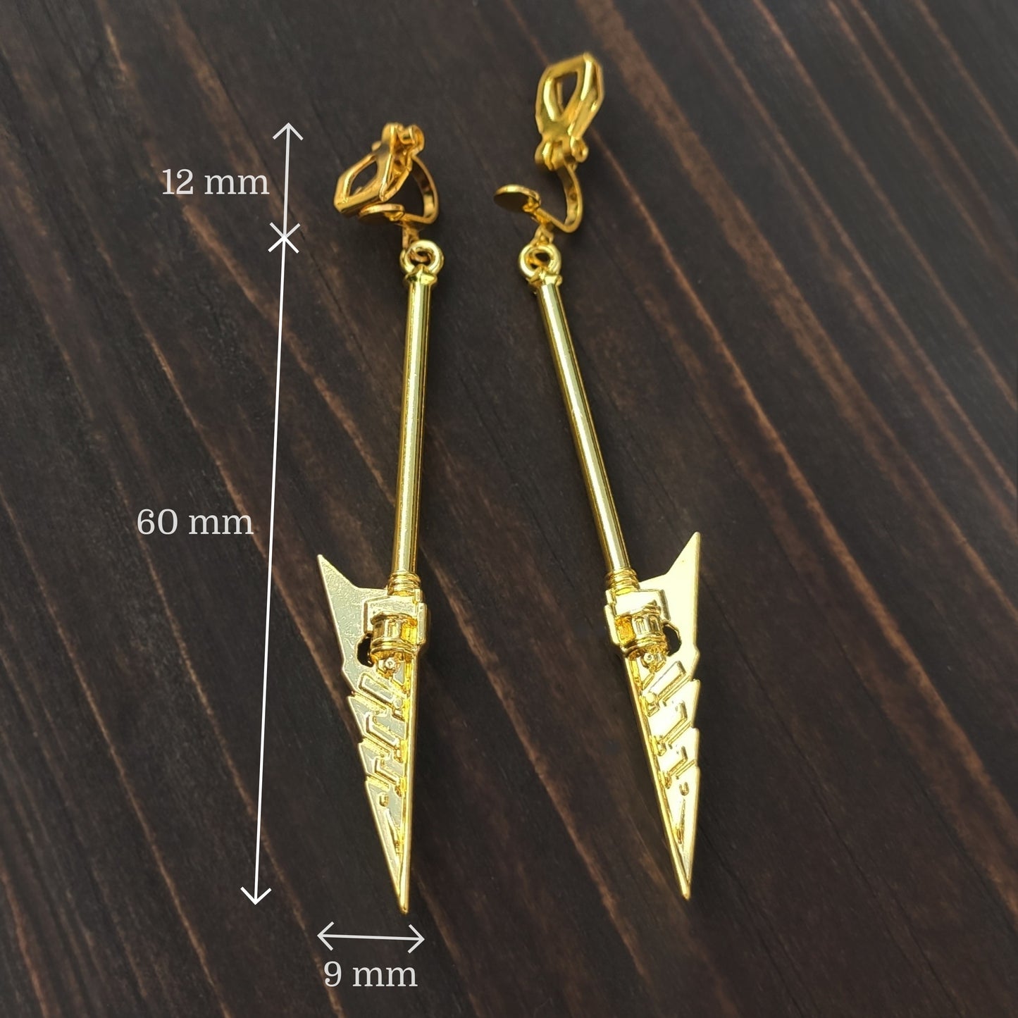 Gold spear-shaped earrings with measurements on a wooden surface