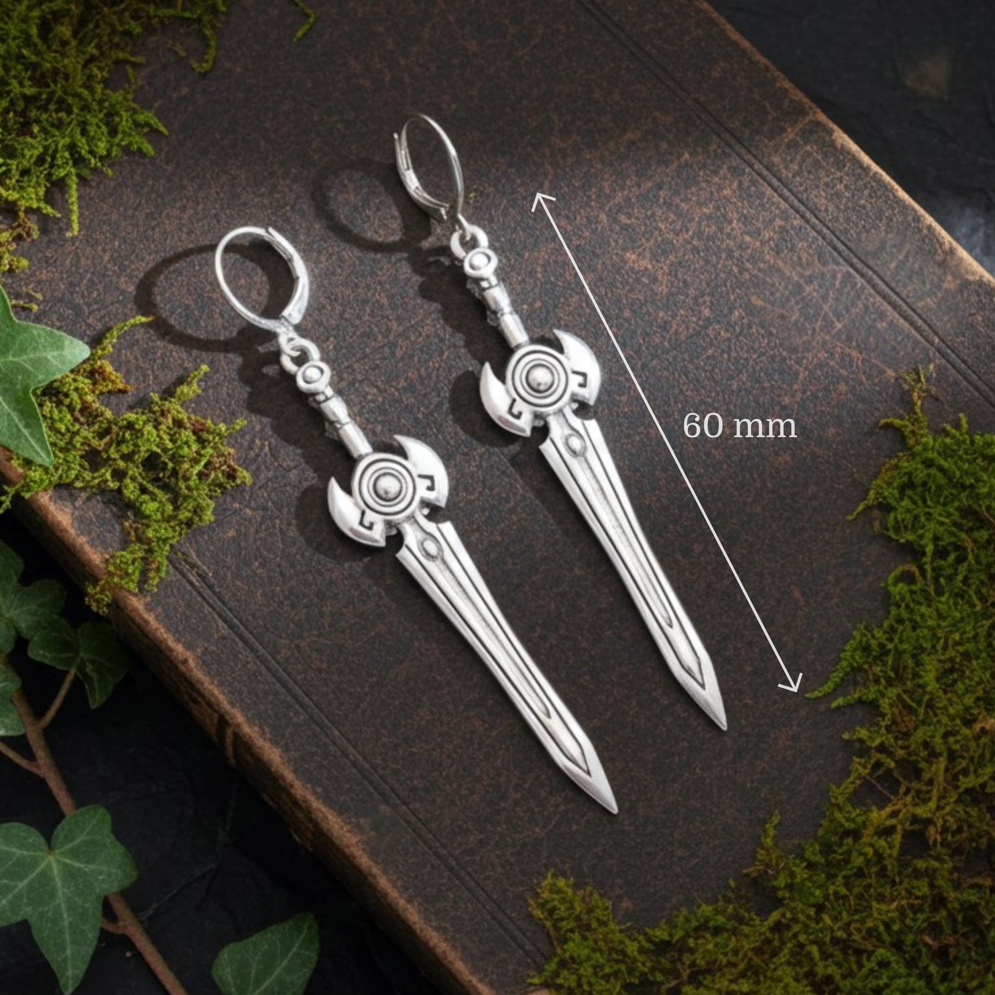 Silver sword earrings on a dark surface with measurements