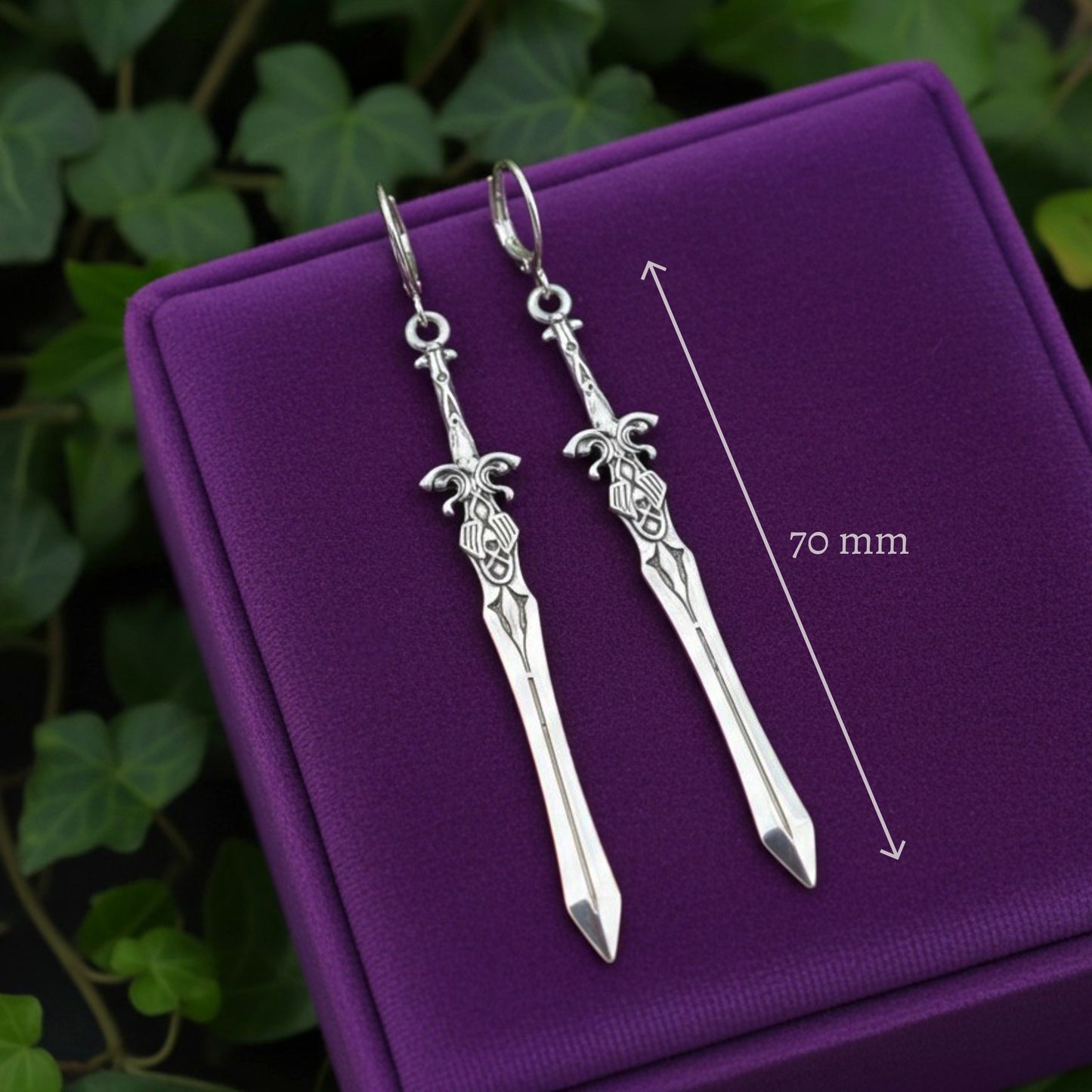 Silver sword-shaped earrings on a purple cushion with a measurement line indicating 70 mm.