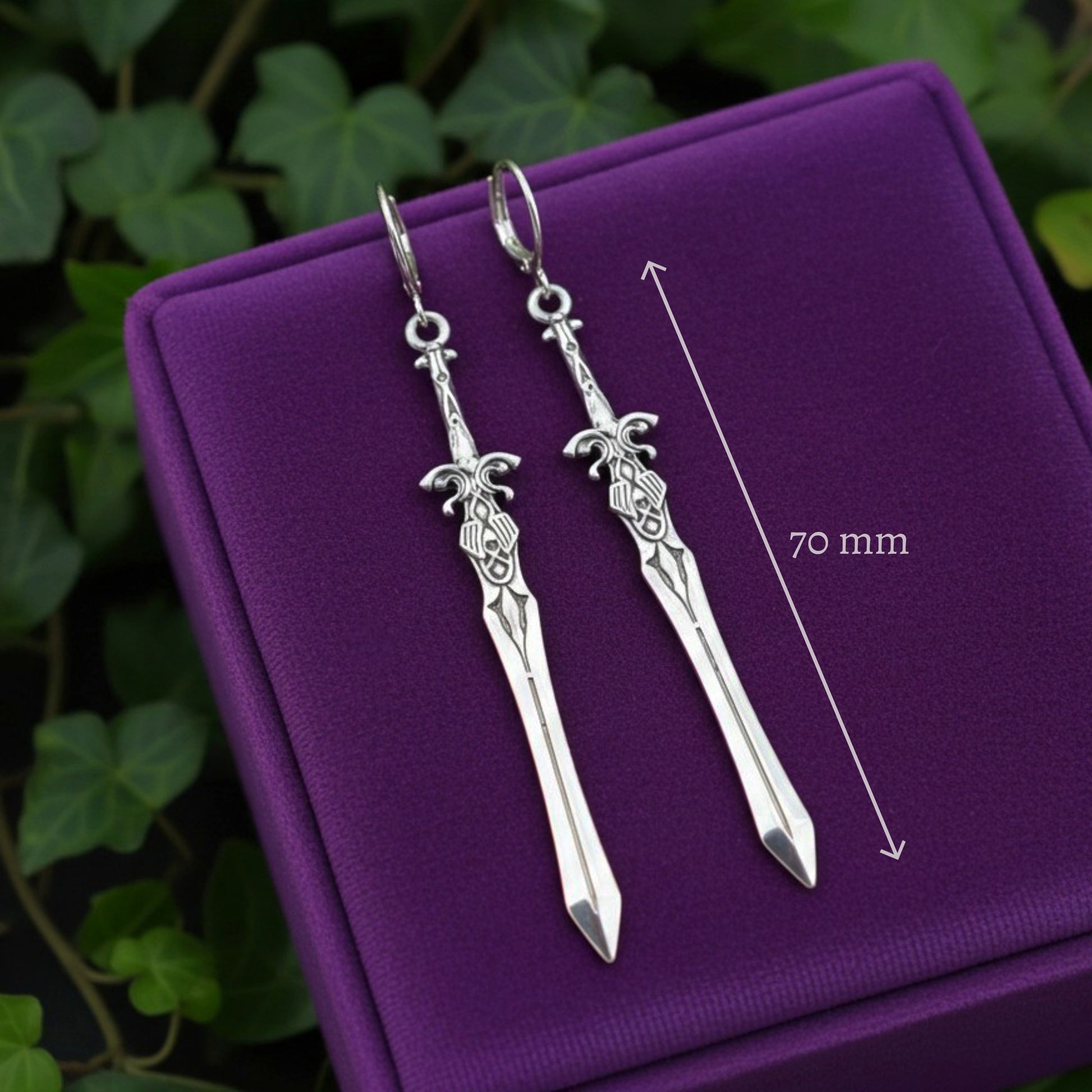 Silver sword-shaped earrings on a purple cushion with a measurement line indicating 70 mm.