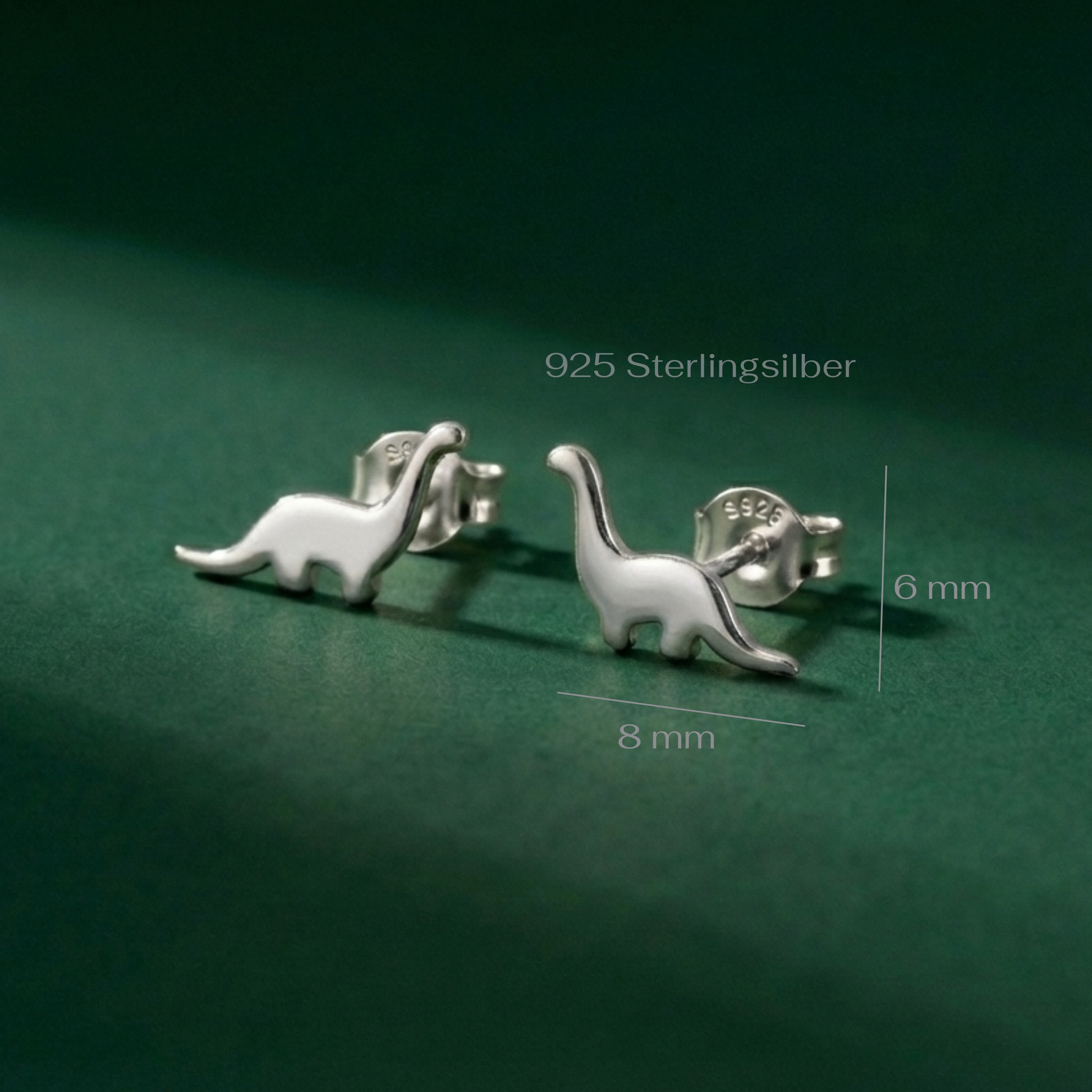 Silver dinosaur-shaped earrings on a green background with measurements.