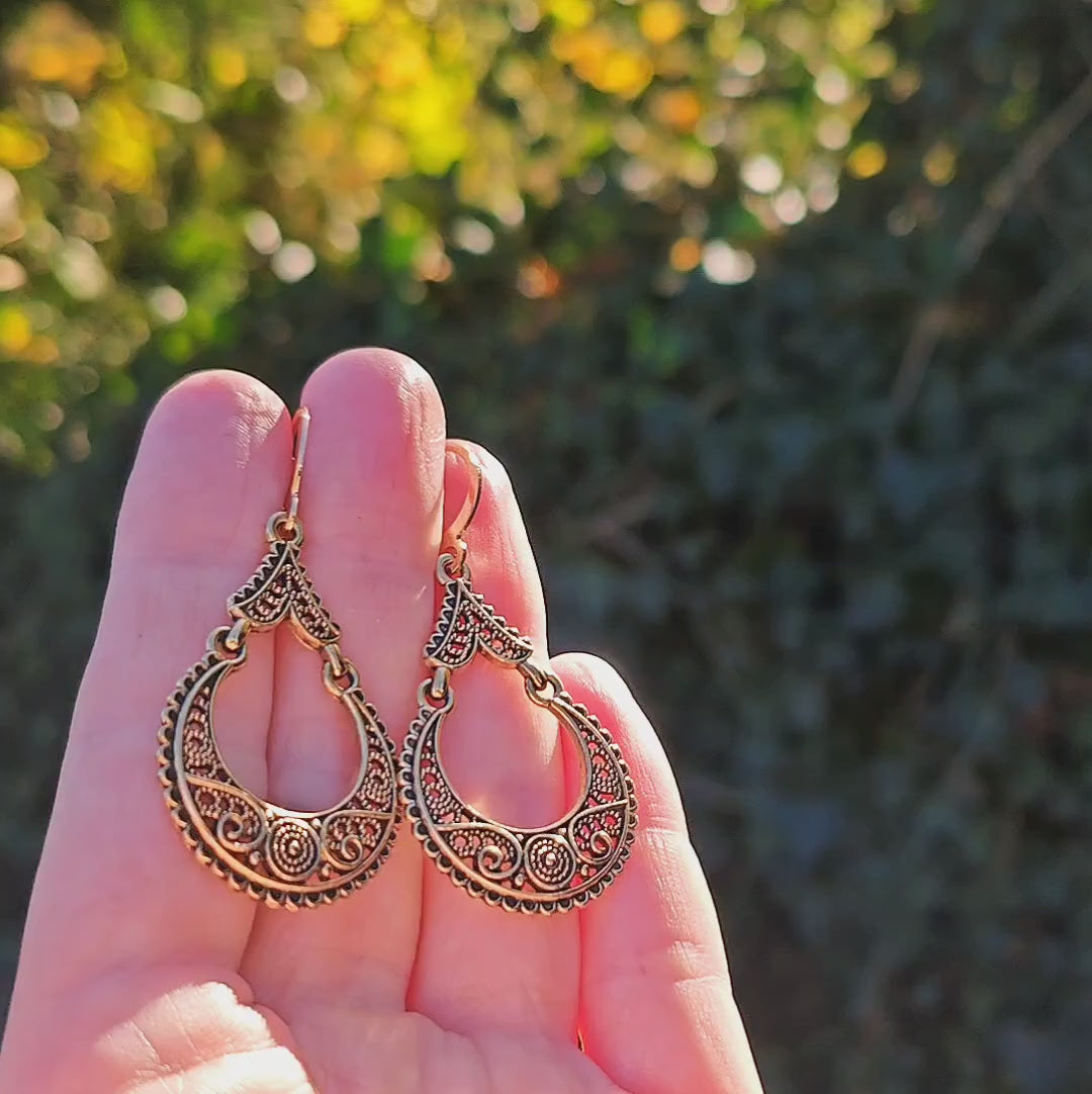 Gold boho dangle earrings shining in sunlight with greenery behind