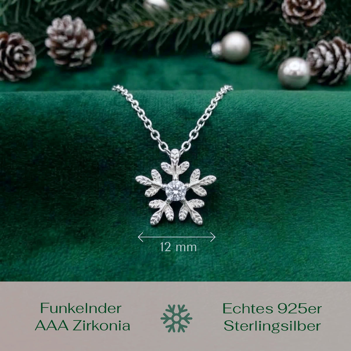 A silver snowflake pendant necklace with a clear center stone, displayed on a dark green velvet surface with pine branches and pinecones in the background. A dimension marker indicates the 12 mm width of the pendant.